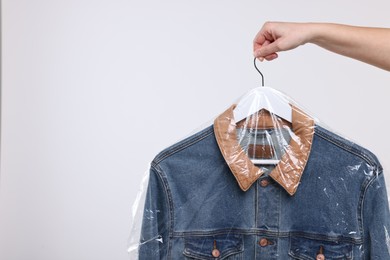 Photo of Dry-cleaning service. Woman holding denim jacket in plastic bag on white background, closeup. Space for text