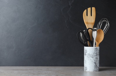 Photo of Holder with kitchen utensils on table against dark background. Space for text