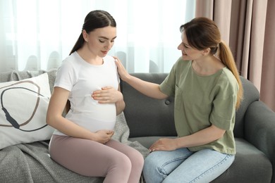 Doula taking care of pregnant woman on sofa at home. Preparation for child birth