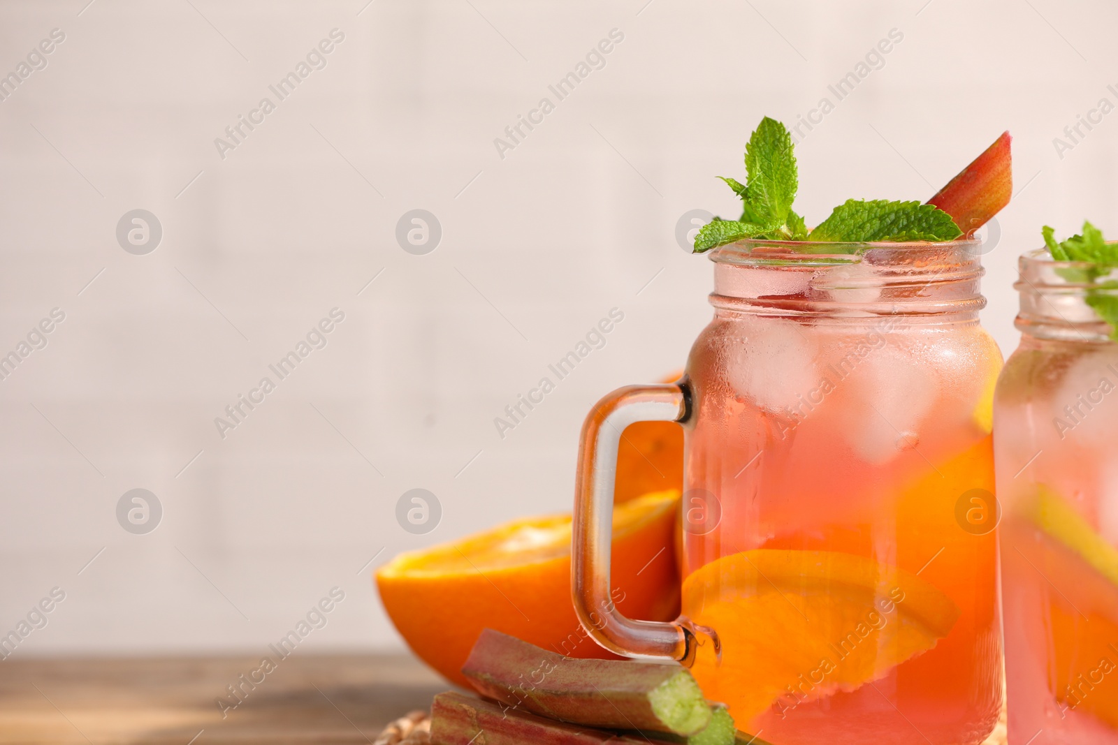 Photo of Mason jars of tasty rhubarb cocktail with citrus fruits on table, closeup. Space for text