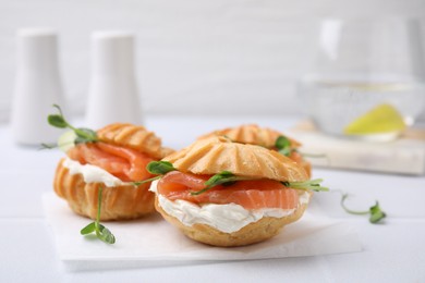 Delicious profiteroles with cream cheese and salmon on white table, closeup