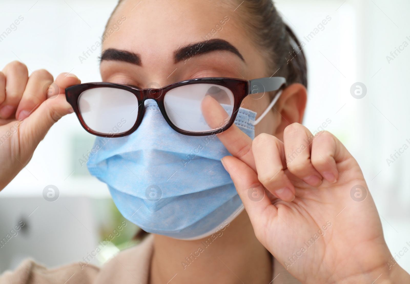 Photo of Woman wiping foggy glasses caused by wearing medical mask indoors, closeup