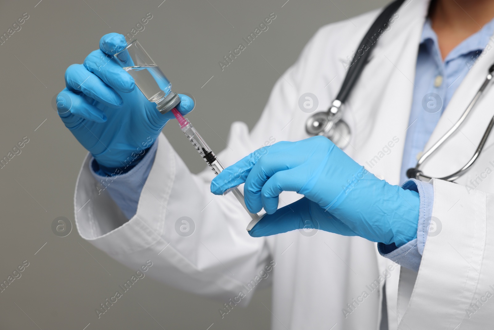 Photo of Doctor filling syringe with medication from glass vial on grey background, closeup