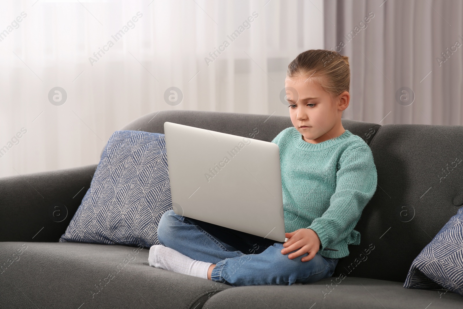 Photo of Little girl using laptop on sofa at home. Internet addiction