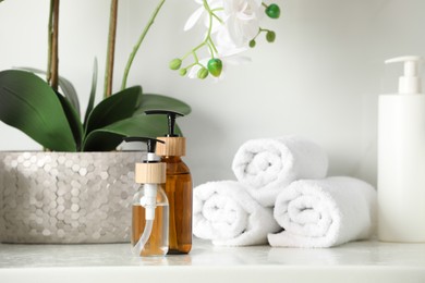 Bottles with dispenser caps, houseplant and towels on white table in bathroom