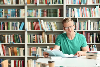 Photo of Pensive young man with books at table in library. Space for text