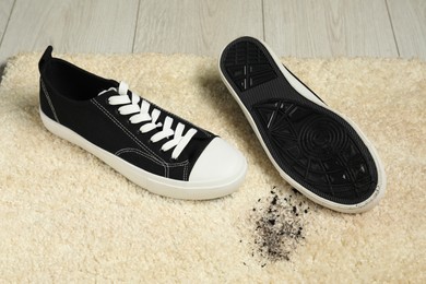 Photo of Black sneakers and mud on beige carpet, closeup