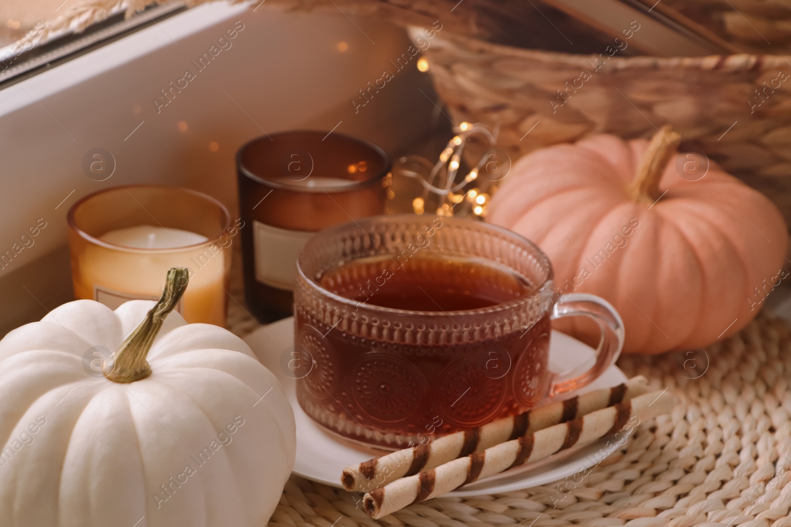 Photo of Cup of hot drink, cookies, candles and pumpkins on window sill indoors