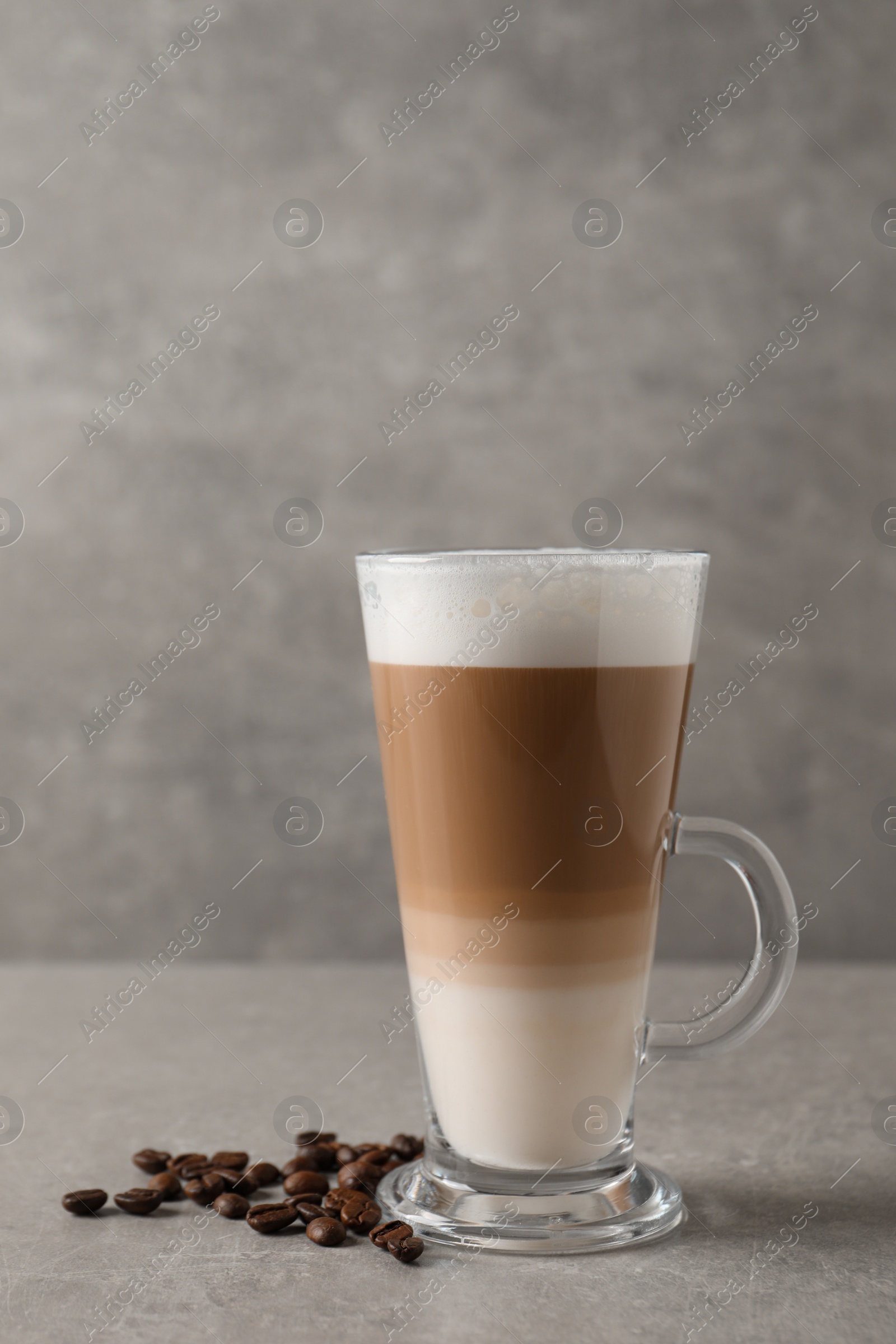 Photo of Glass cup of delicious layered coffee and beans on grey table, space for text