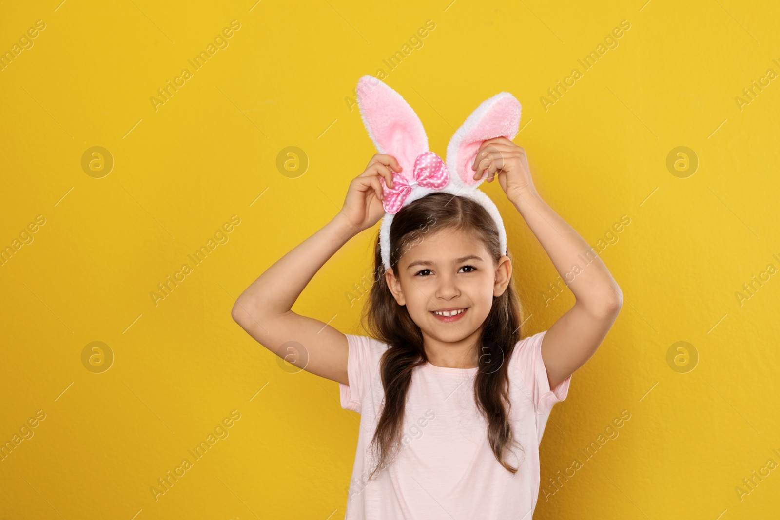 Photo of Portrait of little girl in Easter bunny ears headband on color background