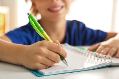 Photo of Little boy doing homework at table indoors, closeup