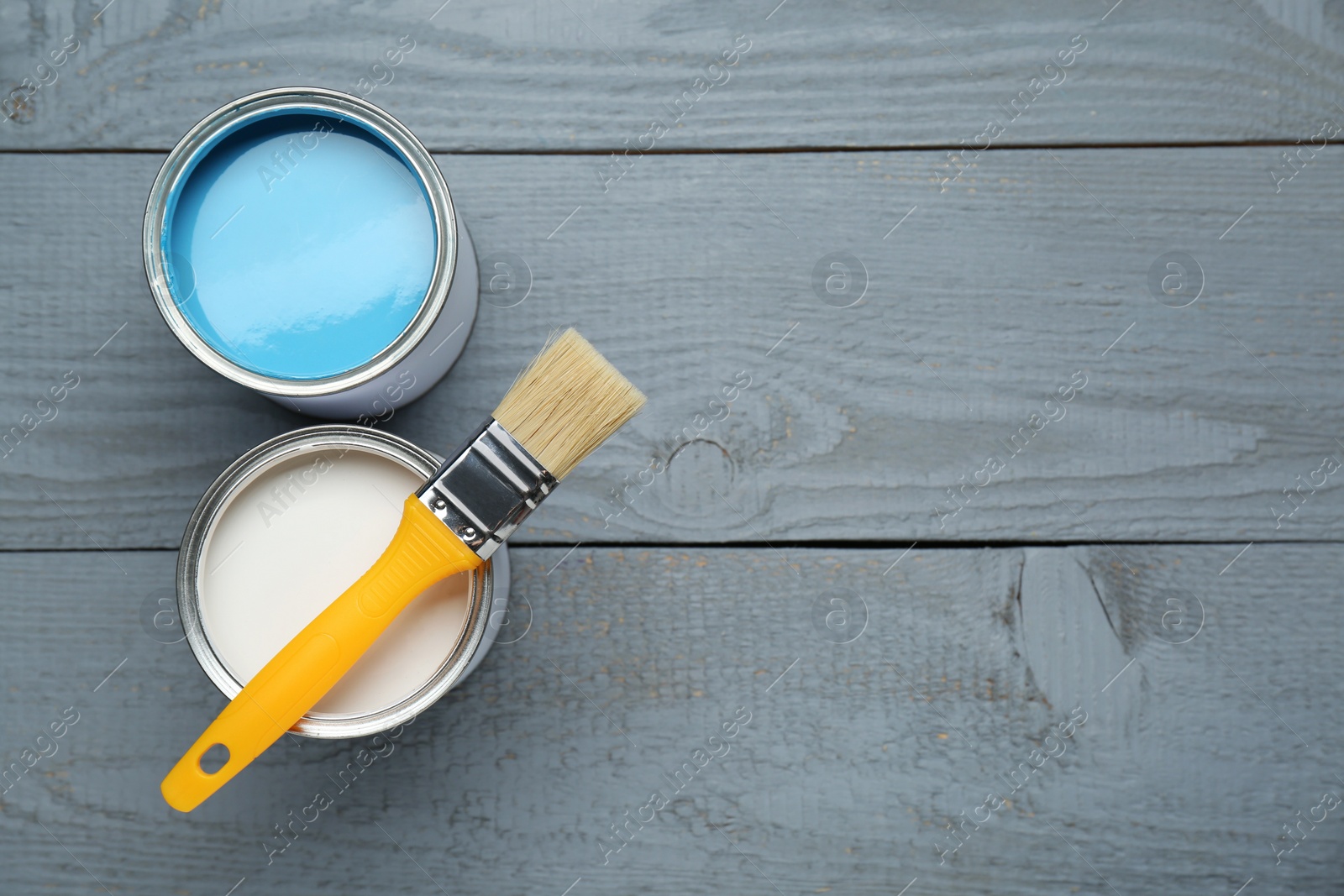 Photo of Cans of colorful paints and brush on grey wooden table, flat lay. Space for text