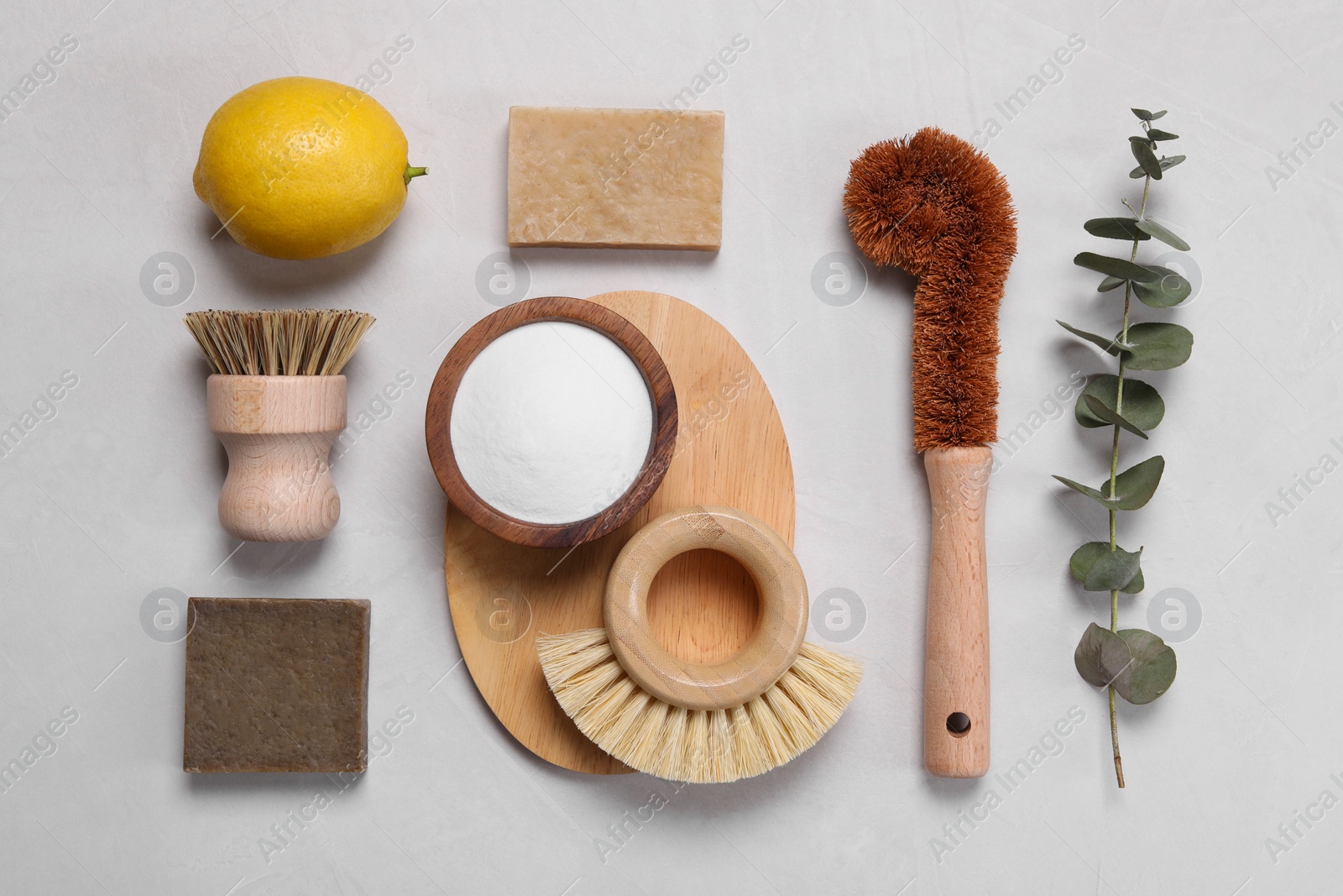 Photo of Cleaning brushes, baking soda, lemon, soap bar and eucalyptus leaves on white table, flat lay