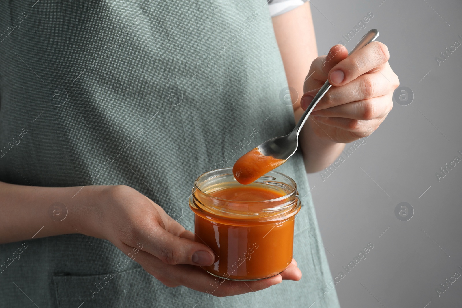 Photo of Woman with delicious persimmon jam on gray background, closeup