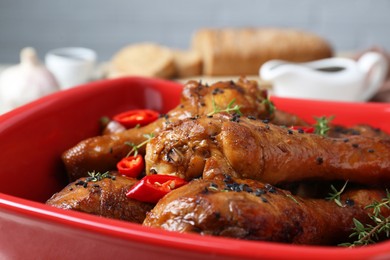 Photo of Chicken legs glazed in soy sauce with black sesame, chili pepper and thyme in red bowl, closeup
