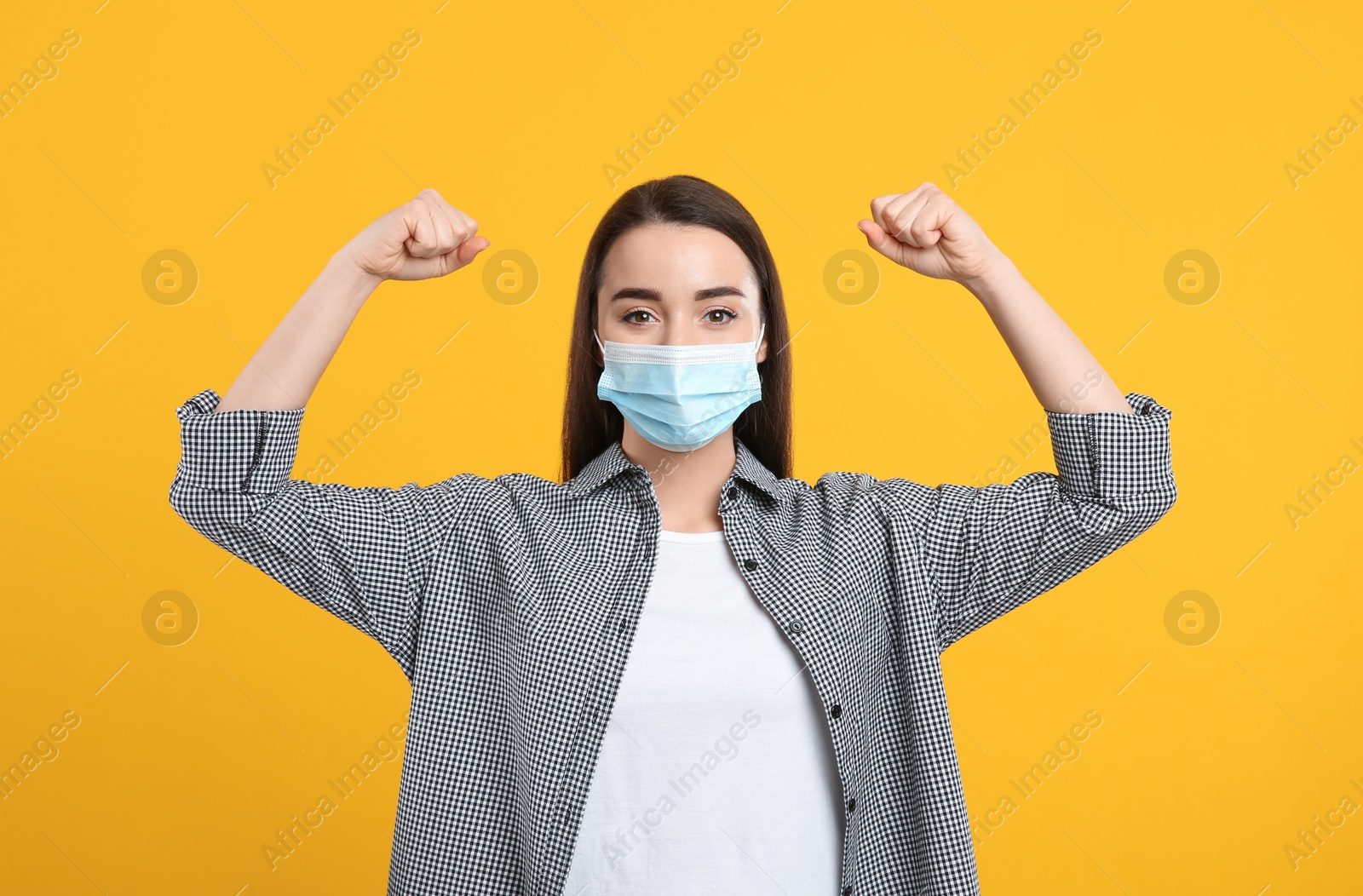 Photo of Woman with protective mask showing muscles on yellow background. Strong immunity concept