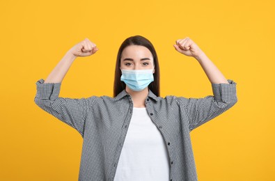 Woman with protective mask showing muscles on yellow background. Strong immunity concept