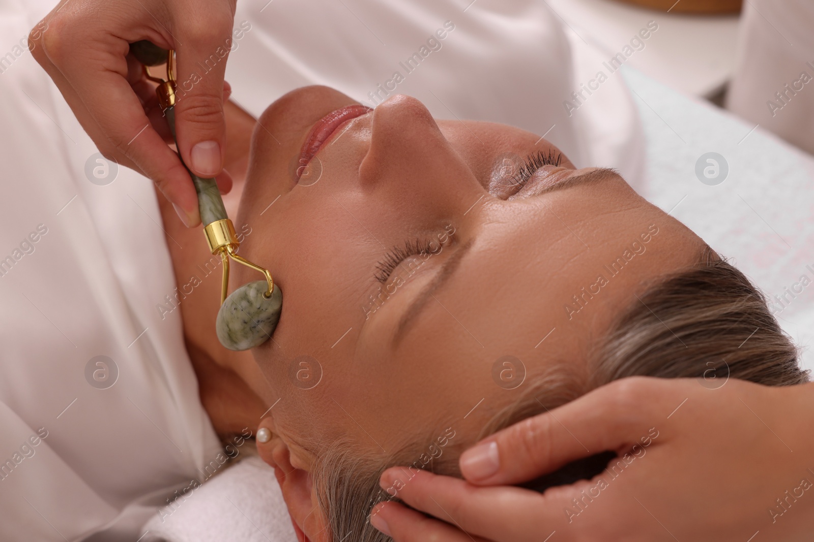 Photo of Woman receiving facial massage with jade roller in beauty salon, closeup