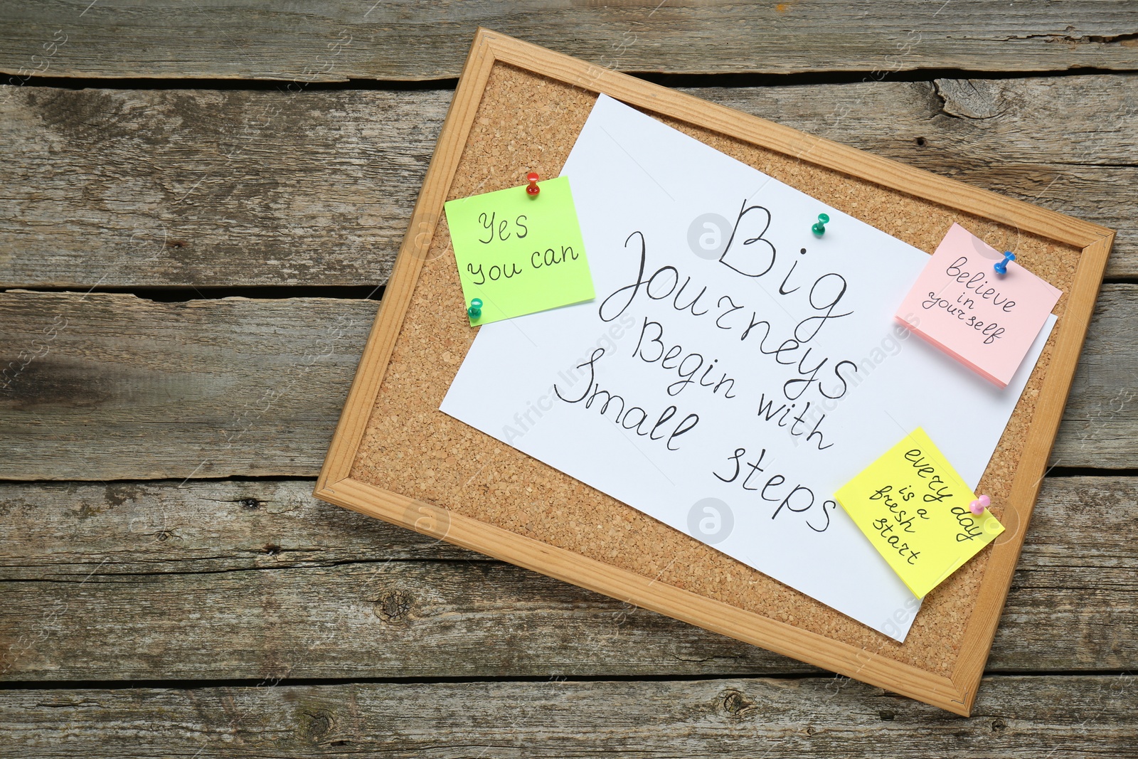 Photo of Corkboard with motivational quotes on wooden table, top view