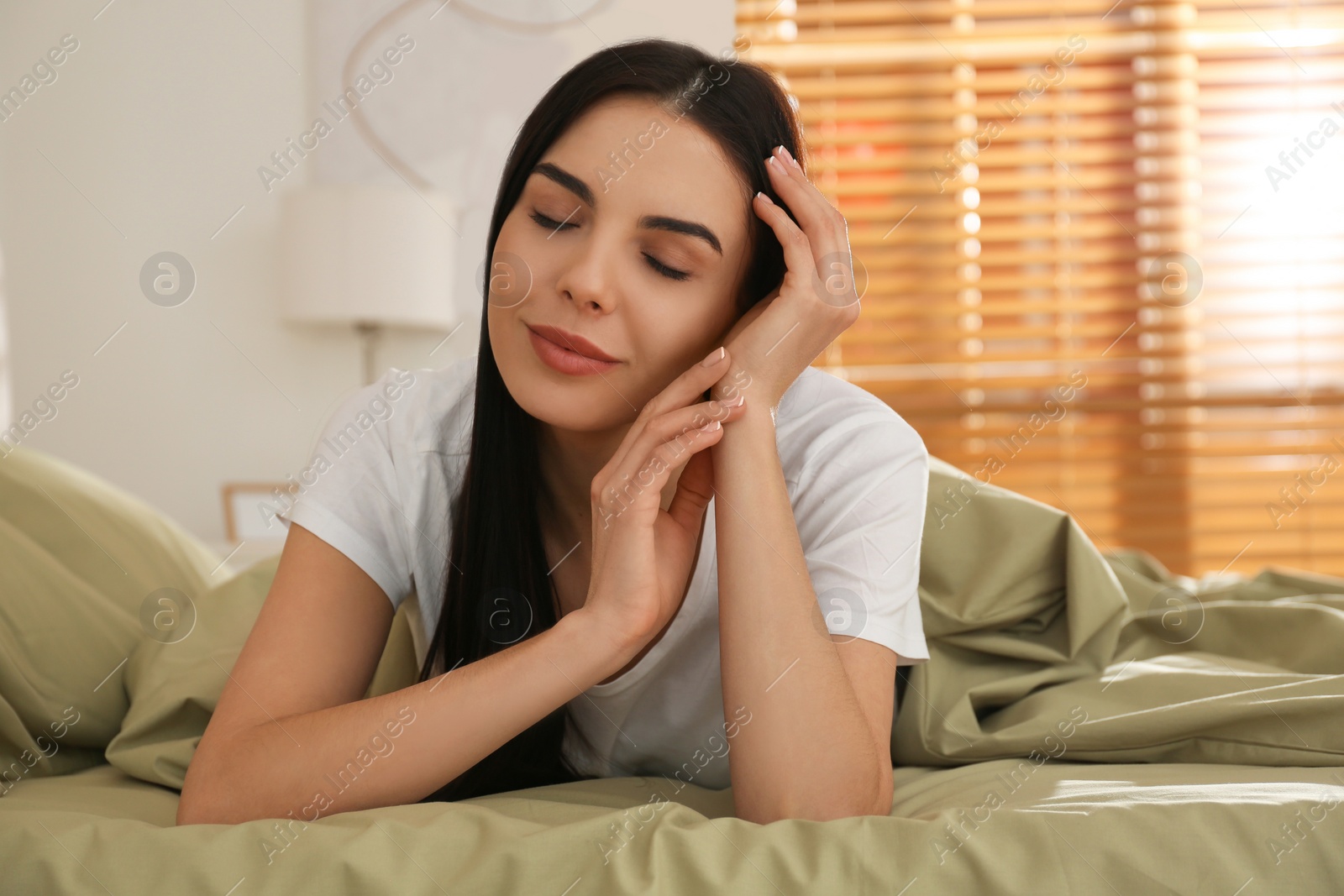 Photo of Young woman lying in bed with green linens at home