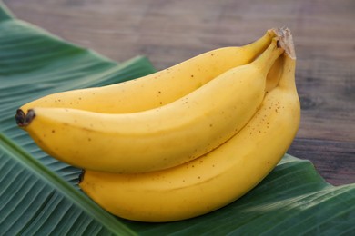 Photo of Delicious bananas and green leaf on wooden table, closeup