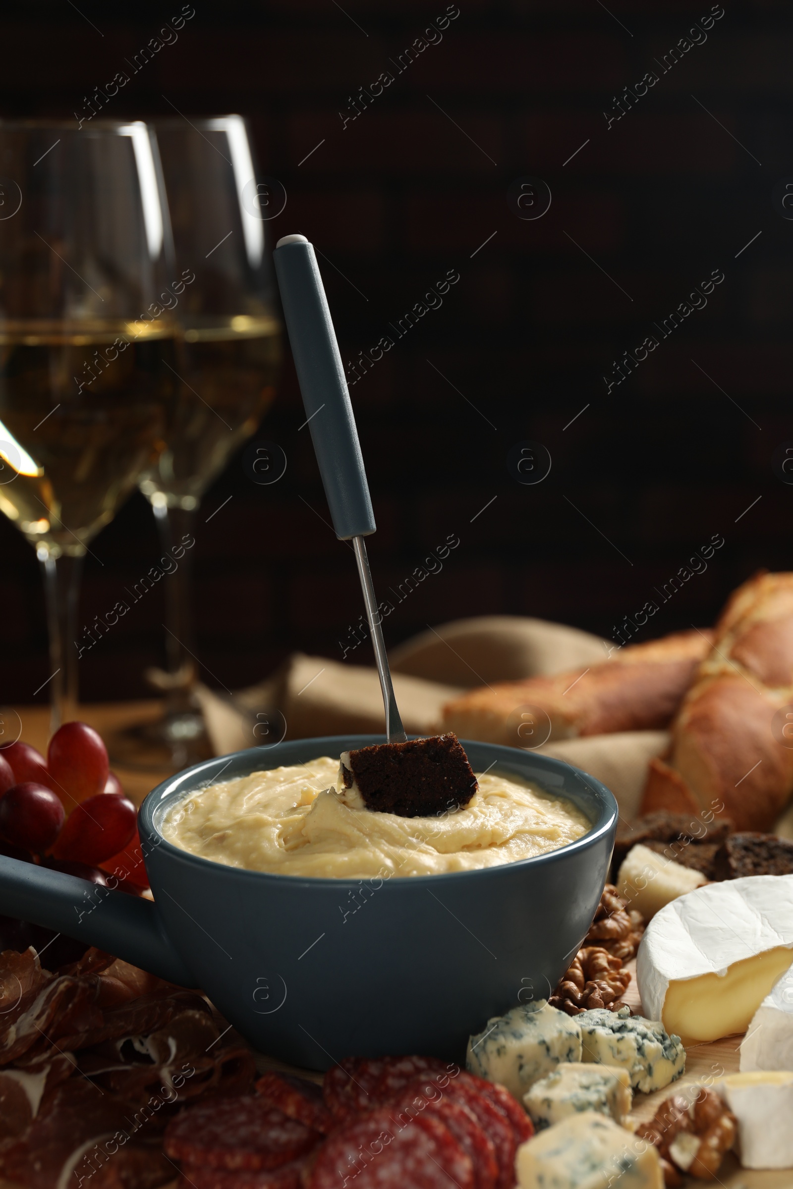 Photo of Fondue pot with tasty melted cheese, fork, different snacks and wine on table