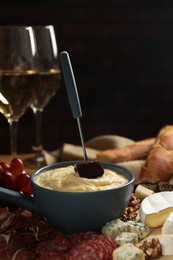 Photo of Fondue pot with tasty melted cheese, fork, different snacks and wine on table