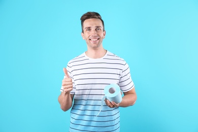 Photo of Young man holding toilet paper roll on color background
