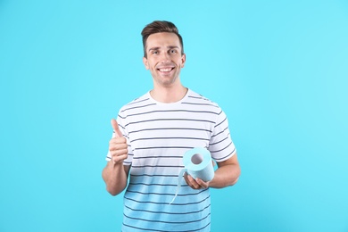 Young man holding toilet paper roll on color background