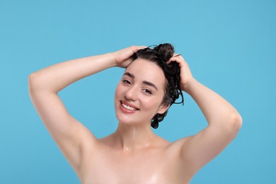 Photo of Portrait of beautiful happy woman washing hair on light blue background