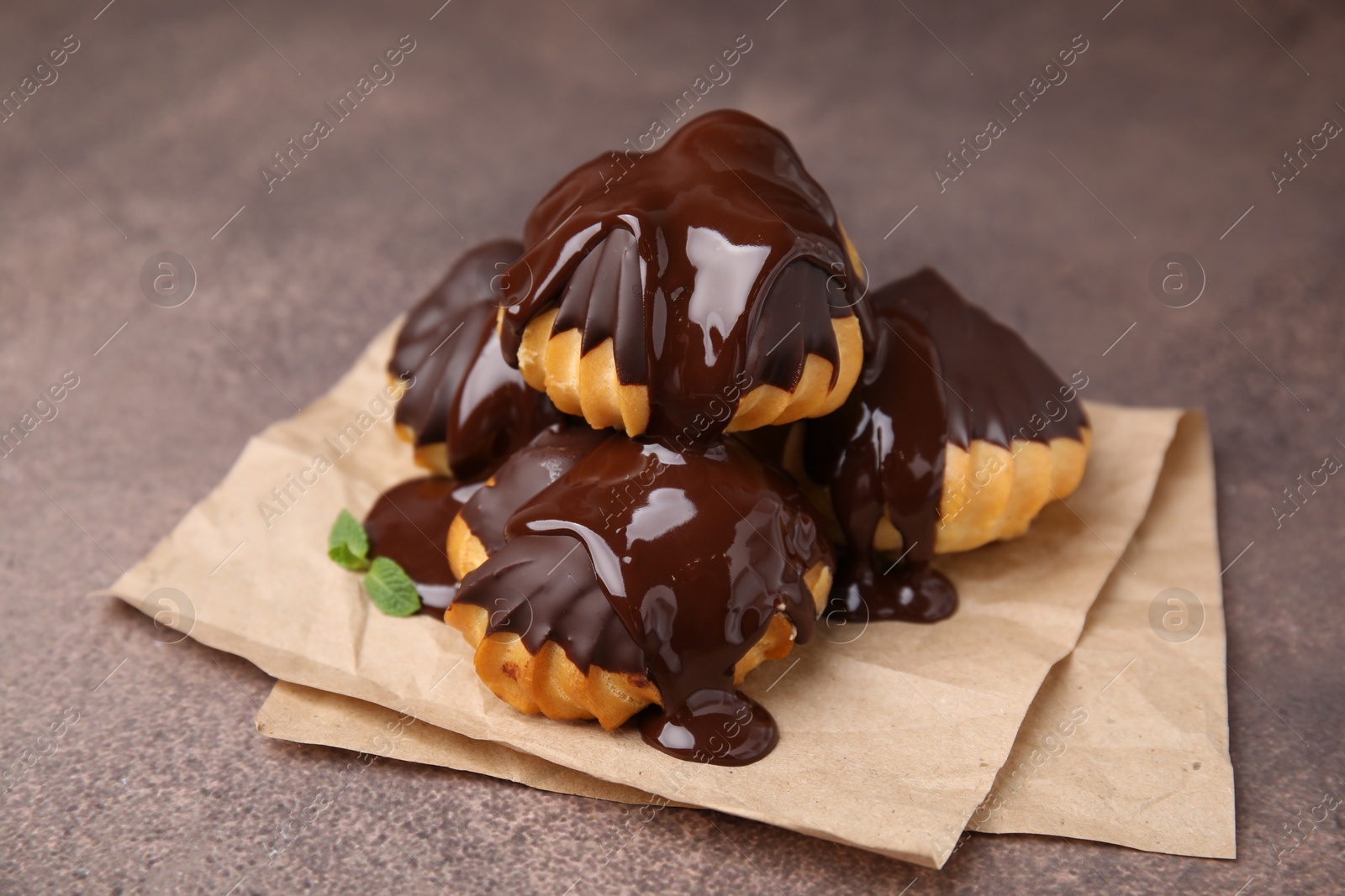 Photo of Delicious profiteroles with chocolate spread and mint on textured table, closeup