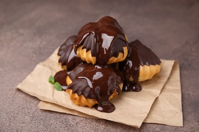 Delicious profiteroles with chocolate spread and mint on textured table, closeup