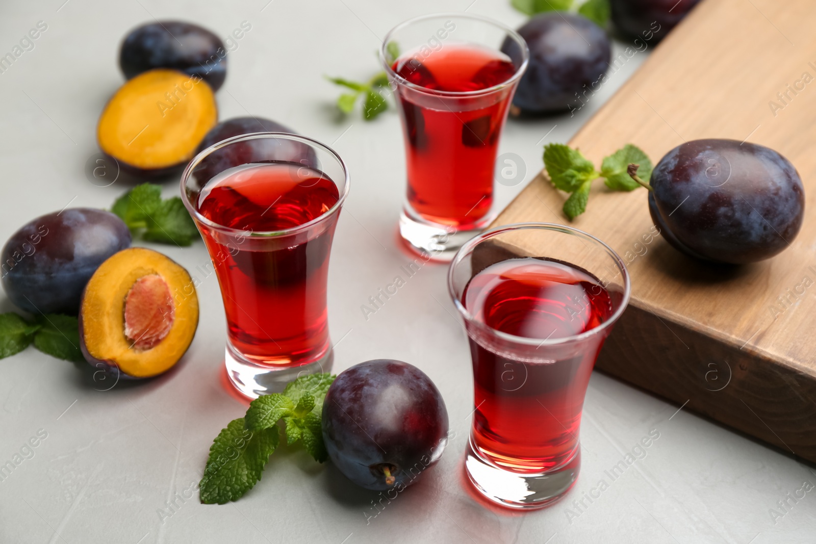 Photo of Delicious plum liquor, mint and ripe fruits on light table. Homemade strong alcoholic beverage