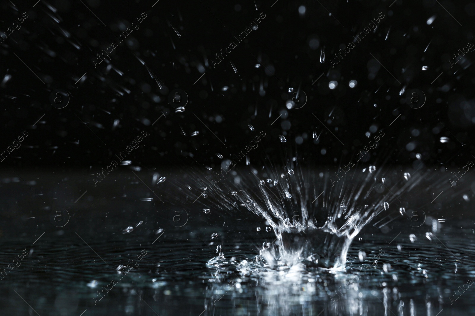 Photo of Rain drop falling down into puddle on dark background