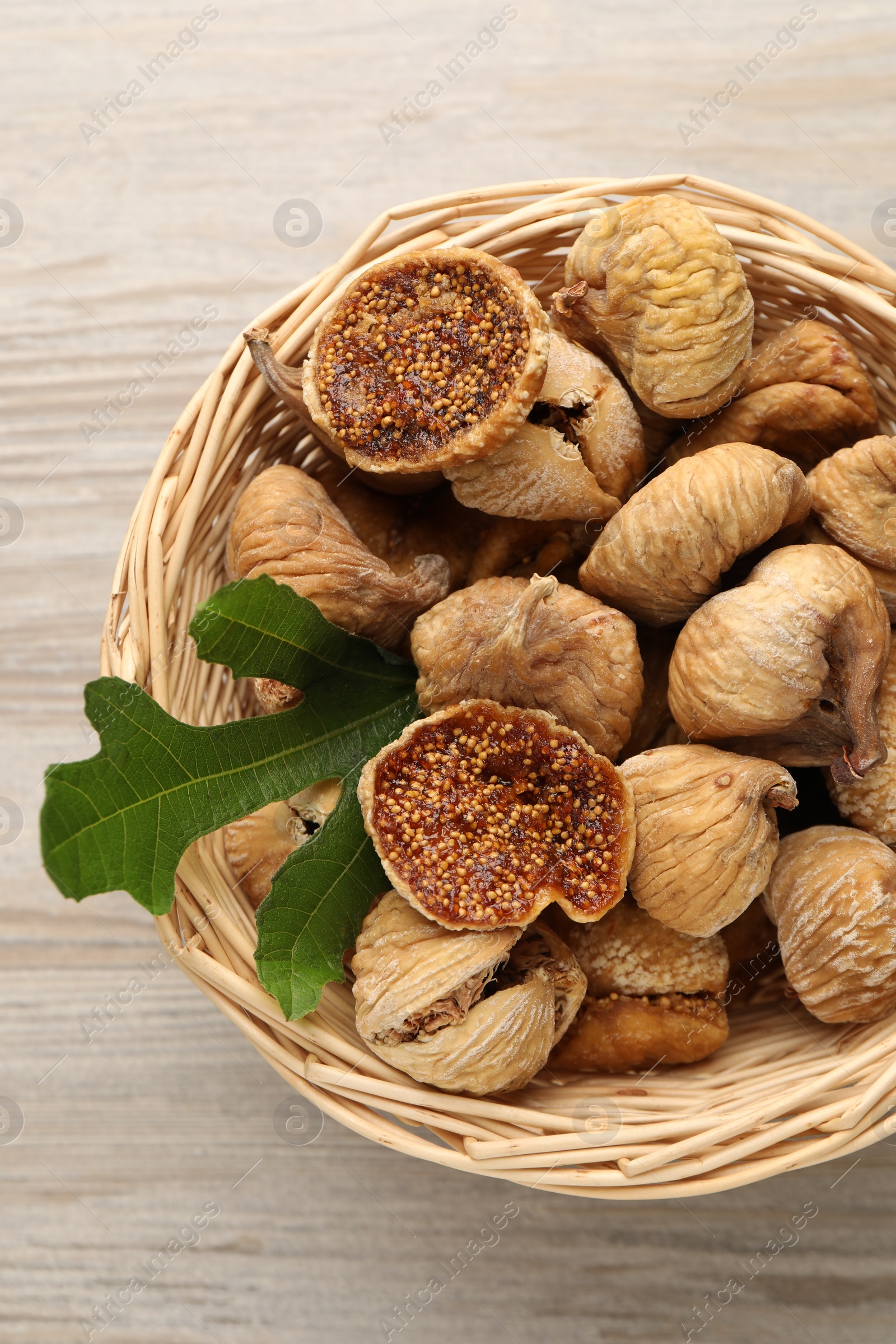 Photo of Wicker basket with tasty dried figs and green leaf on light wooden table, top view