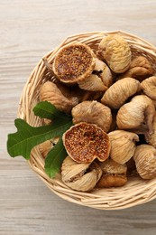 Wicker basket with tasty dried figs and green leaf on light wooden table, top view