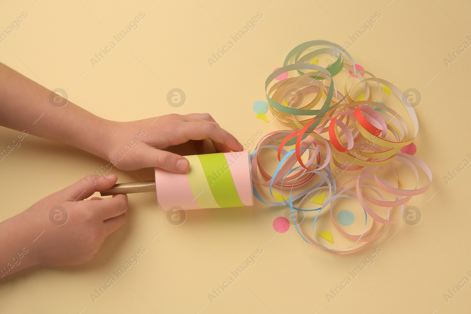 Photo of Woman holding party popper with serpentine and confetti on beige background, top view