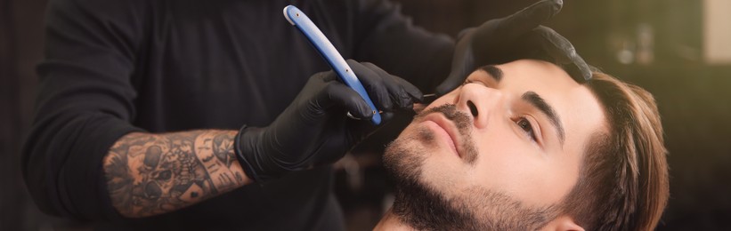 Image of Professional hairdresser shaving client with straight razor in barbershop. Banner design