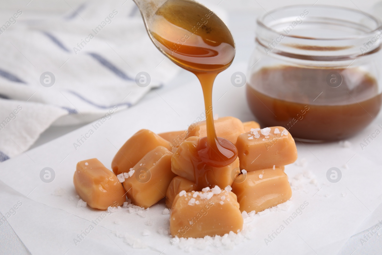 Photo of Pouring delicious salted caramel on candies on white table