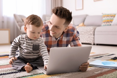 Photo of Young father with his cute little son using laptop at home