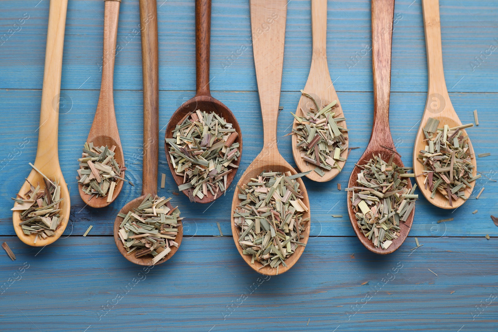 Photo of Spoons with aromatic dried lemongrass on light blue wooden table, flat lay