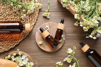 Flat lay composition with chamomile essential oil and flowers on wooden background.