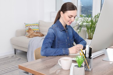 Woman working at desk and cat lying on sofa in room. Home office