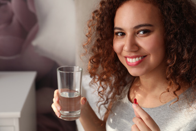 Photo of African-American woman with glass of water and vitamin pill at home