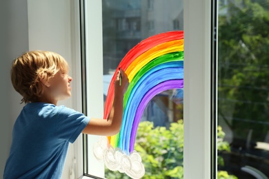 Photo of Little boy drawing rainbow on window indoors. Stay at home concept