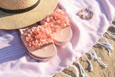 Photo of Blanket with stylish slippers, bracelet and straw hat on sandy beach, closeup