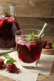 Photo of Glass of delicious iced hibiscus tea with straw and dry flowers on wooden table