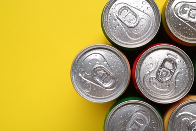 Photo of Energy drinks in wet cans on yellow background, top view. Space for text