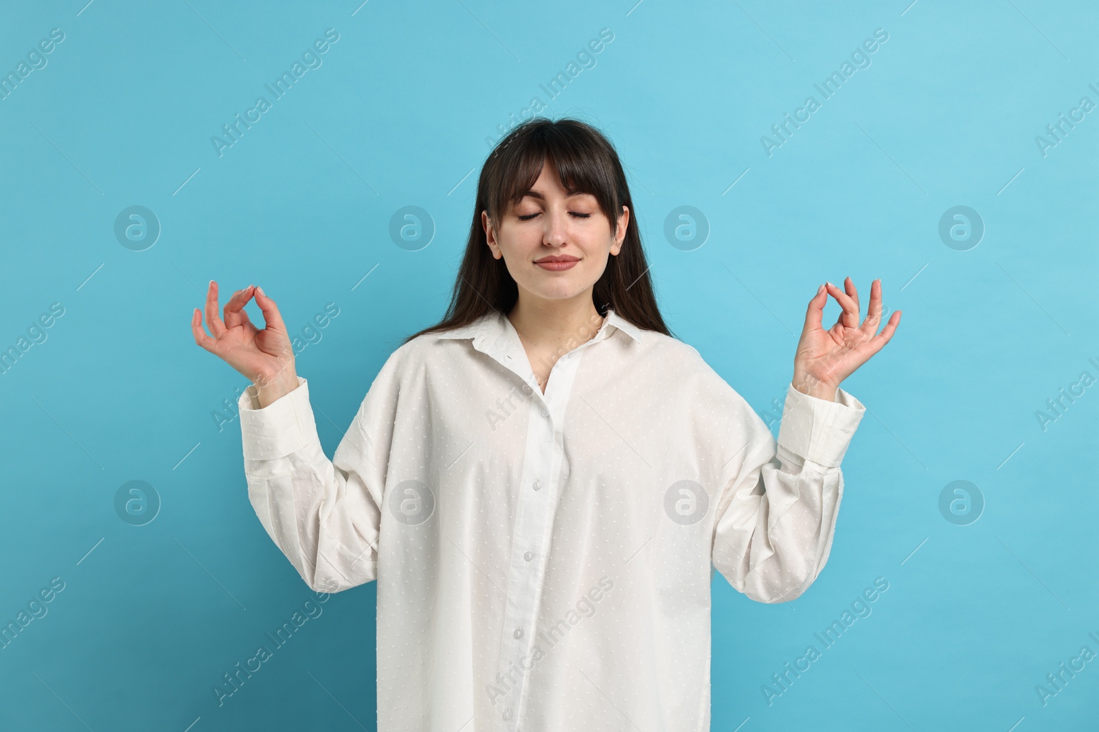 Photo of Woman in pyjama meditating on light blue background