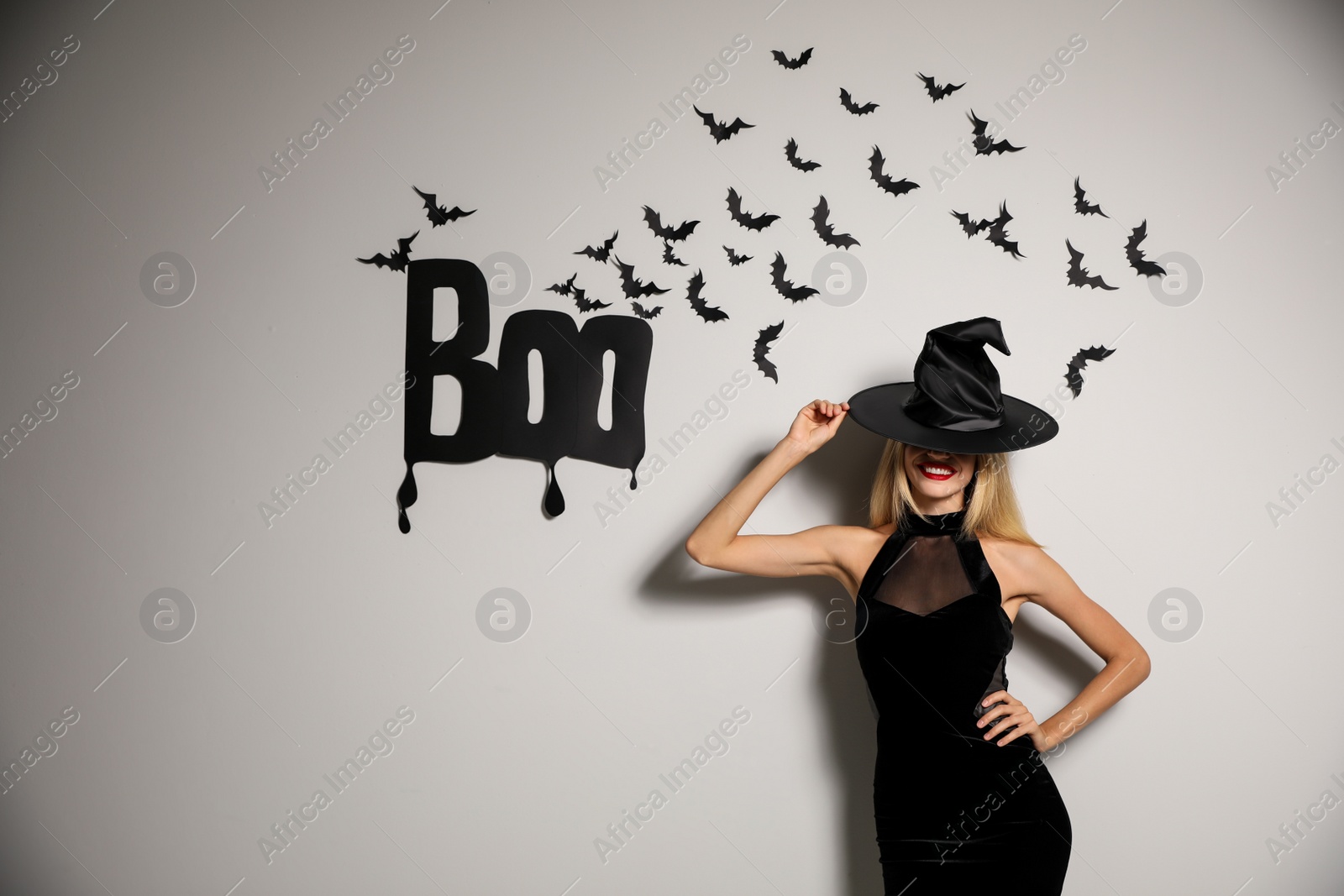 Photo of Woman in witch hat posing near white wall decorated for Halloween